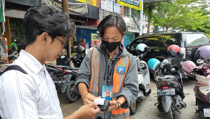 Juru parkir menggunakan alat transaksi berbasis QR Code di Makassar.