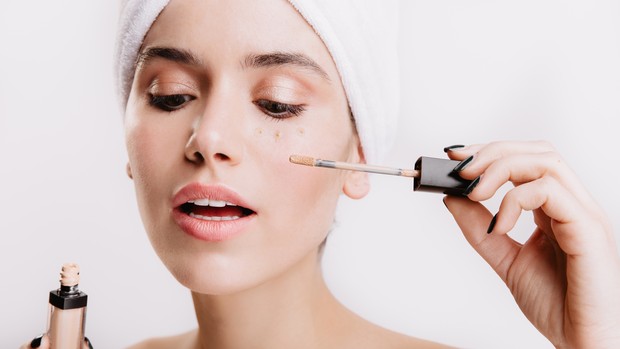 Memakai concealer untuk menutupi noda wajah pada makeup cantik perempuan usia 40-an.