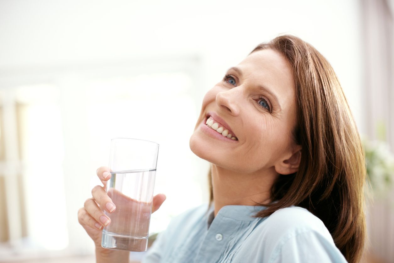 A mature woman looking away happily as she holds a glass of water