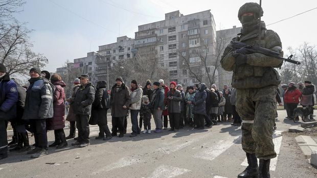 A Russian army soldier stands next to local residents who queue for humanitarian aid delivered during Ukraine-Russia conflict, in the besieged southern port of Mariupol, Ukraine March 23, 2022.  REUTERS/Alexander Ermochenko