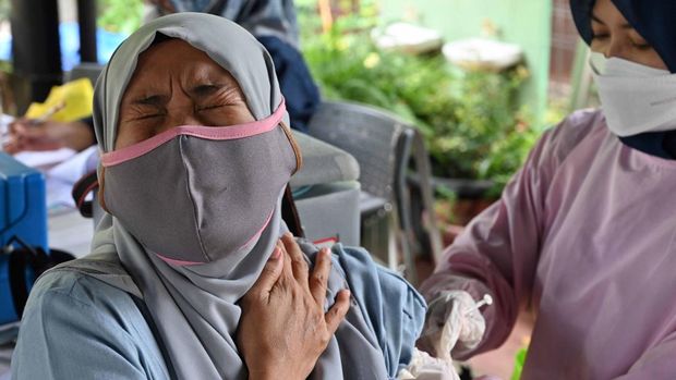 A woman (L) reacts while receiving a Pfizer booster vaccine for the Covid-19 coronavirus in Jakarta on March 29, 2022. - The government has accelerated vaccination programmes ahead of Eid al-Fitr in May, when many people leave the capital and return back to their hometowns. (Photo by ADEK BERRY / AFP)