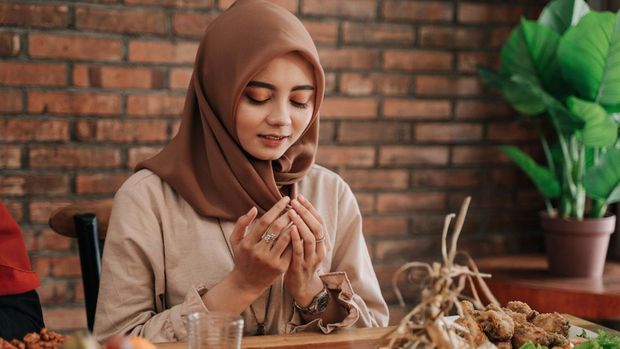 beautiful muslim woman open her palm and pray before eating