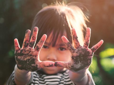 Cute little girl smiles and shows off her muddy hands while planting trees in the backyard. Educational concept outside the school fence.