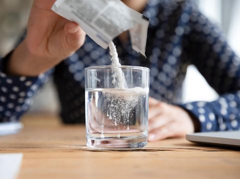 Close up young indian woman pouring soluble anti-influenza powder in glass of water. Sick millennial girl student feeling unwell, relieving grippe fever flu symptoms, high temperature, headache.