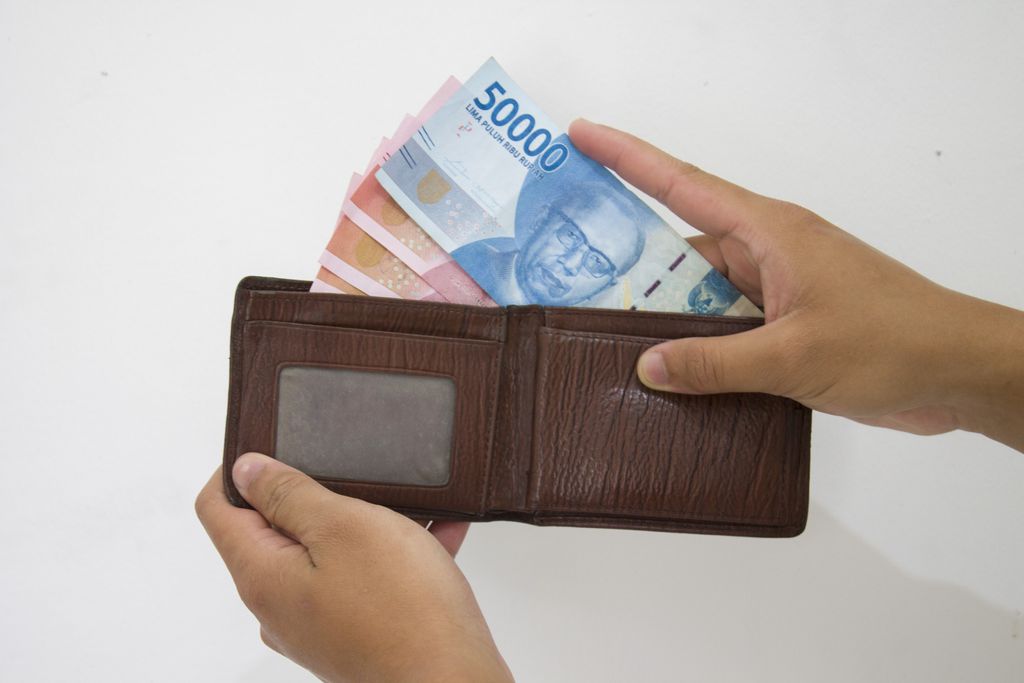 Hand holding Indonesian Rupiah (IDR) Red 100,000 bank notes currency from leather wallet on white background.