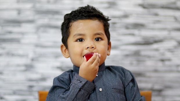 A young boy is enjoying a piece of homemade jelly at home in Malaysia. He is wearing 'baju Melayu' (traditional Muslim man attire).
