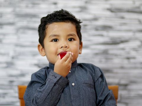 A young boy is enjoying a piece of homemade jelly at home in Malaysia. He is wearing 'baju Melayu' (traditional Muslim man attire).