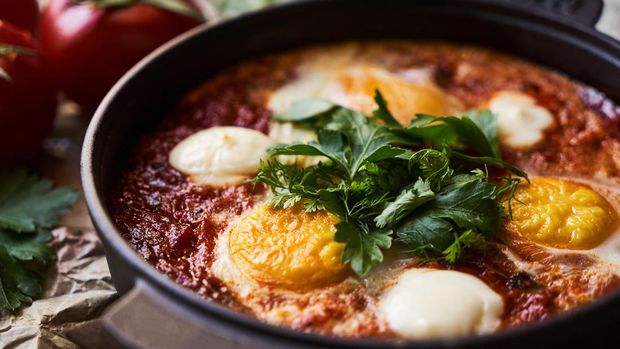 Pan of Fried Eggs with Tomatoes, Sweet Peppers and Coriander. Healthy vegetarian breakfast food concept. Shakshuka with eggs, tomatoes and parsley in a frying pan, close-up.