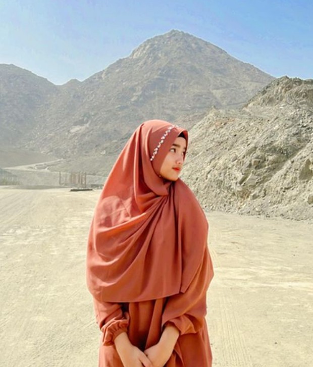 Fuji mengenakan setelan hijab dan gamis syar'i berwarna cokelat bata saat menjalankan ibadah Umrah