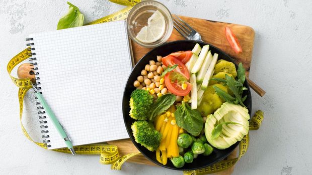 Vegan healthy balanced diet concept. Vegetarian buddha bowl with blank notebook and measuring tape. hickpeas, broccoli, pepper, tomato, spinach, arugula and avocado in plate on white background. Top view