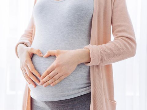 Pregnant young woman holding hand in shape of heart on her belly