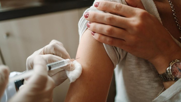 Young doctor giving COVID 19 vaccine to young woman at home