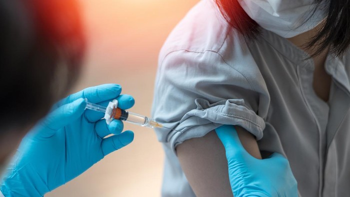 Young doctor giving COVID 19 vaccine to young woman at home