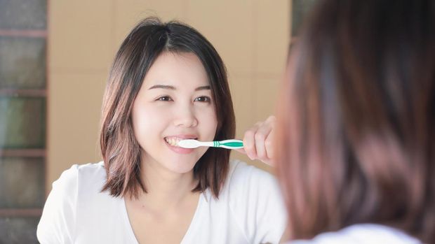 Young woman brushing her teeth at mirror. After awakening