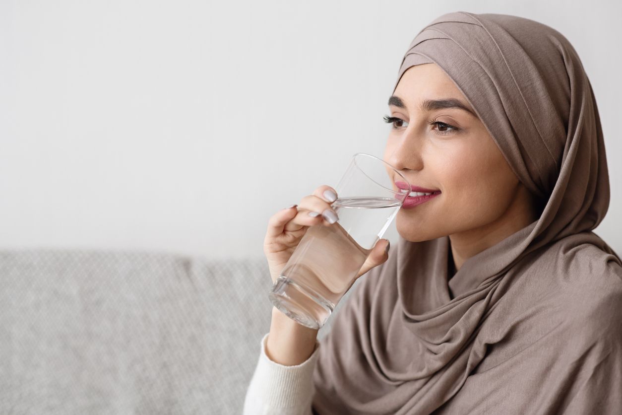 Young muslim girl in hijab drinking water from glass at home, closeup portrait, free space