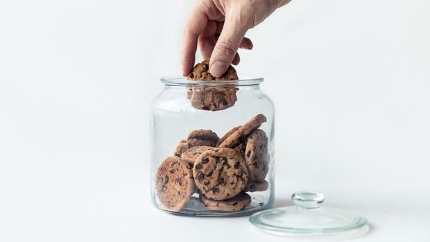 Shot of a hand taking cookies from a glass jar on white background.