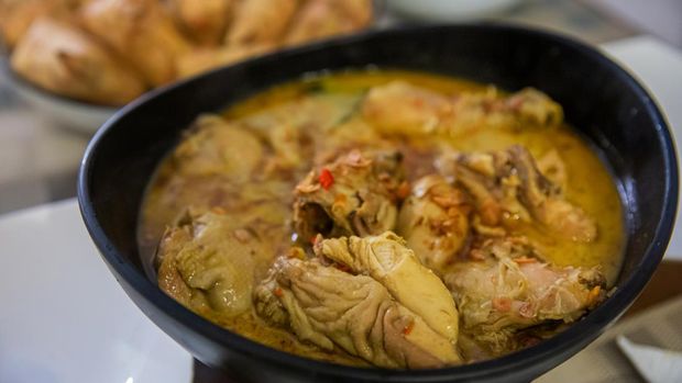 Close up shot of traditional Javanese chicken and coconut curry (Opor Ayam) in a black bowl above dining table, as Ramadan meal main course.