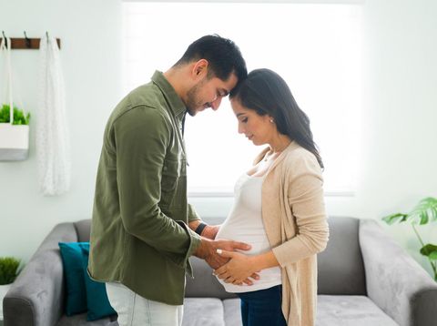 Side view of a future mom and dad holding hands with their heads together. Beautiful beaming couple looking and gazing at the pregnant woman's belly