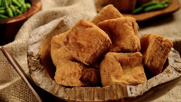 Tahu Sumedang, the popular street food of deep-fried bean curd from Sumedang, West Java. Served in a natural wooden bowl. Further back in the background, there are partial view of a bowl of green chili peppers and a small plate of individual serving of the bean curd.