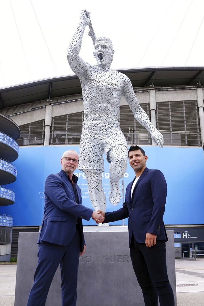 Sculptor Andy Scott, left, shakes hands with Sergio Aguero in front of the statue he made of Manchester City Club legend Aguero, outside of the Etihad Stadium, Manchester, to commemorate the tenth anniversary of the Club's first Premier League title and the iconic '93:20' moment, Friday May 13, 2022. (Martin Rickett/PA via AP)