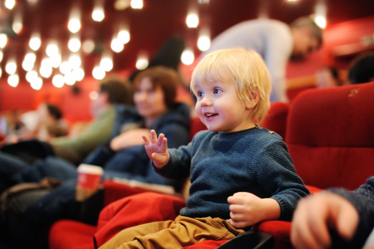 Cute toddler boy watching cartoon movie in the cinema. Leisure/entertainment for family with kids.