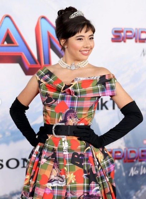 Xochitl Gomez mengenakan plaid dress bermotif loud print, serta mahkota kecil sebagai aksesoris kepala