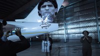 Seorang pria memegang jersey bertuliskan angka 10 dan Maradona saat berpose di sebelah pesawat bertema sang legenda sepakbola itu di sebuah pangkalan militer di Moron, yang berada di pinggiran Buenos Aires, Argentina, Rabu (25/5/2022) waktu setempat.