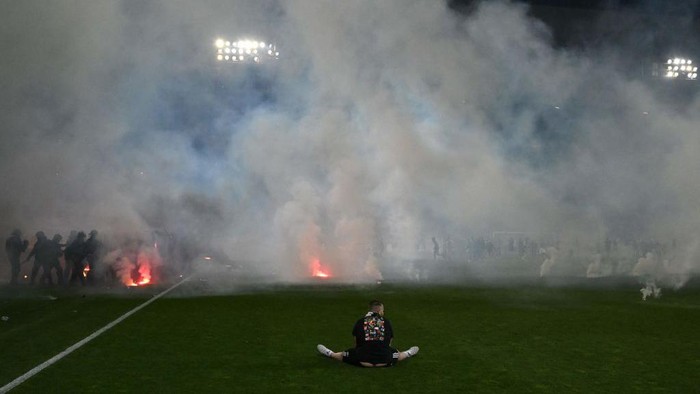 Saint Etienne A football fan sits on the pitch as riot police officers in background clash with Saint-Etienne's fans who invaded the pitch after being defeated by Auxerre at the end of the French L1-L2 play-off second leg football match between AS Saint-Etienne and AJ Auxerre at the Geoffroy Guichard Stadium in Saint-Etienne, central-eastern France on May 29, 2022. (Photo by JEAN-PHILIPPE KSIAZEK / AFP) (Photo by JEAN-PHILIPPE KSIAZEK/AFP via Getty Images)