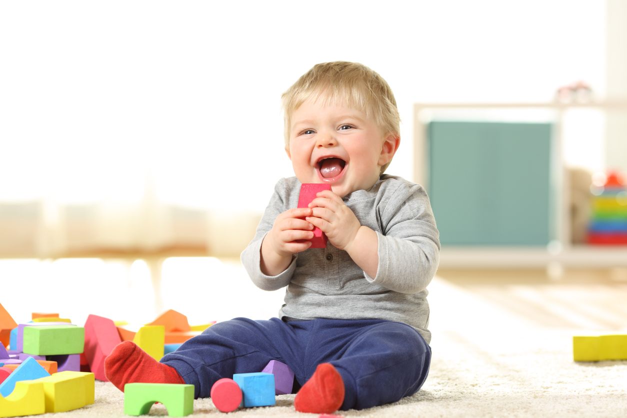 Baby laughing and playing with colorful toys sitting on a carpet at home