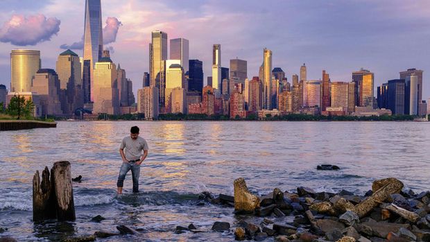 Nyalang Edisi 4 Juni 2022 A man checks his footing as he wades through the Morris Canal Outlet in Jersey City, N.J., as the sun sets on the lower Manhattan skyline of New York City, Tuesday, May 31, 2022. (AP Photo/J. David Ake)