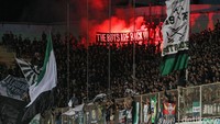 Para suporter menyalakan kembang api di tribun penonton sembari membentangkan spanduk.