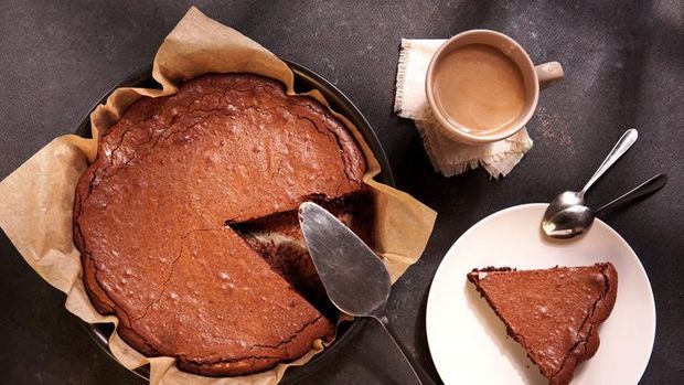 Homemade dark chocolate cake brownie in baking pan, mug with tea or coffee, chocolate on dark table with window light. Delicious bitter sweet and fudge.  Flat lay, top view, vintage style.
