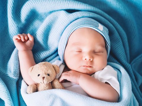 Newborn baby sleep at first days of life. Portrait of new born child boy one week old sleeping peacefully with a cute soft toy in crib in cloth background.