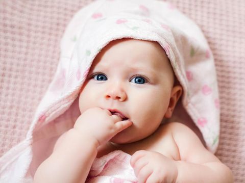Authentic portrait of 4 months baby girl wrapped in hooded towel after bath. Horizontal image in soft pink tones.