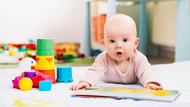 Adorable 6 months old baby looking and reading a book. Baby playing with colorful toys at home. Happy child playing and discovery. Early development, learning and education of kid