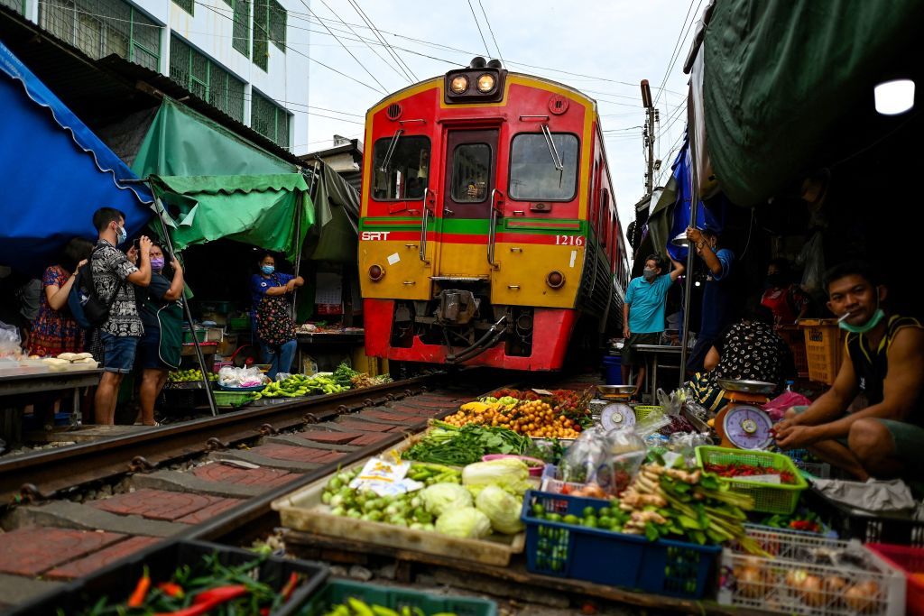 TOPSHOT - This photograph taken on June 4, 2022 shows a passenger train passing through the Mae Klong railway market in Samut Songkhram province, around 80 kms (50 miles) southwest of Bangkok. - Six times a day at the market, local customers and foreign tourists scramble into nooks and crannies while vendors calmly move their woven baskets of goods away from the tracks and close their umbrellas. - TO GO WITH Thailand-tourism-railway-market,FOCUS by Lisa MARTIN (Photo by Manan VATSYAYANA / AFP) / TO GO WITH Thailand-tourism-railway-market,FOCUS by Lisa MARTIN (Photo by MANAN VATSYAYANA/AFP via Getty Images)
