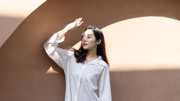 Portrait of a beautiful Asian woman with healthy skin. She uses a sun protection hand that hits her face to protect against UV that has caused her face to dull.