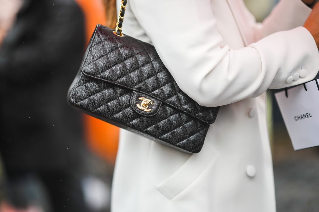 PARIS, FRANCE - OCTOBER 05: A guest wears a white long coat, a white shopping bag from Chanel, a black shiny grained leather shoulder bag from Chanel, outside Chanel, during Paris Fashion Week - Womenswear Spring Summer 2022, on October 05, 2021 in Paris, France. (Photo by Edward Berthelot/Getty Images)