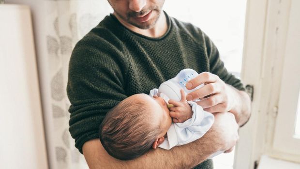 Unrecognizable man feeding newborn baby boy with milk in baby bottle, close up