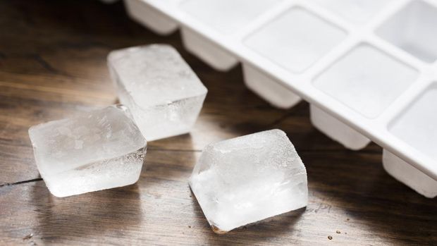 Ice cube tray filled with ice cubes and three lose ice cubes against dark wood.