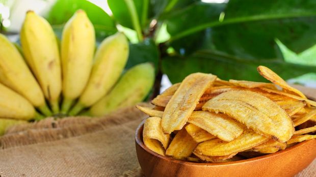 Pile Banana Chips In Bowl Against Banana Fruit Background.