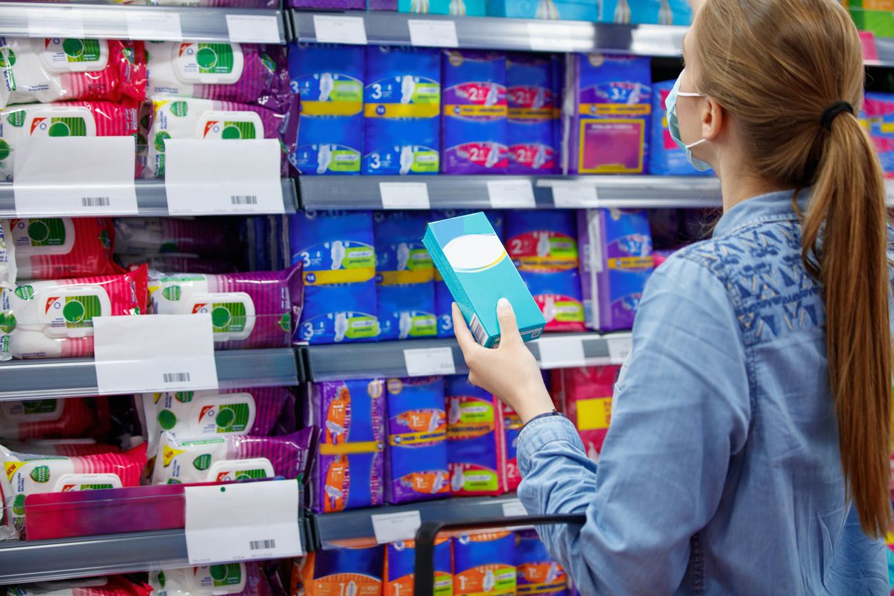Young woman wearing protective face mask, buying tampons or sanitary napkins during covid-19 outbreak, blank label on tampon package
