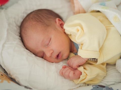 Cute newborn baby boy sleeping peacefully lying in bed at home