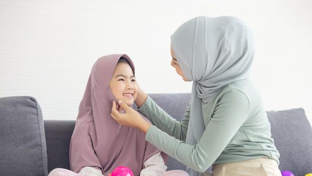 Portrait of happy lovely family arabic muslim mother and little muslim girls child with hijab dress smiling and having fun hugging and kissing together in living room