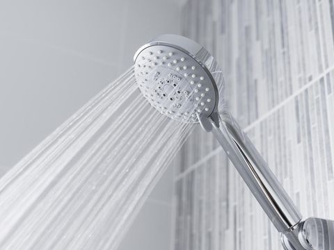 Fresh shower behind wet glass window with water drops splashing. Water running from shower head and faucet in modern bathroom.