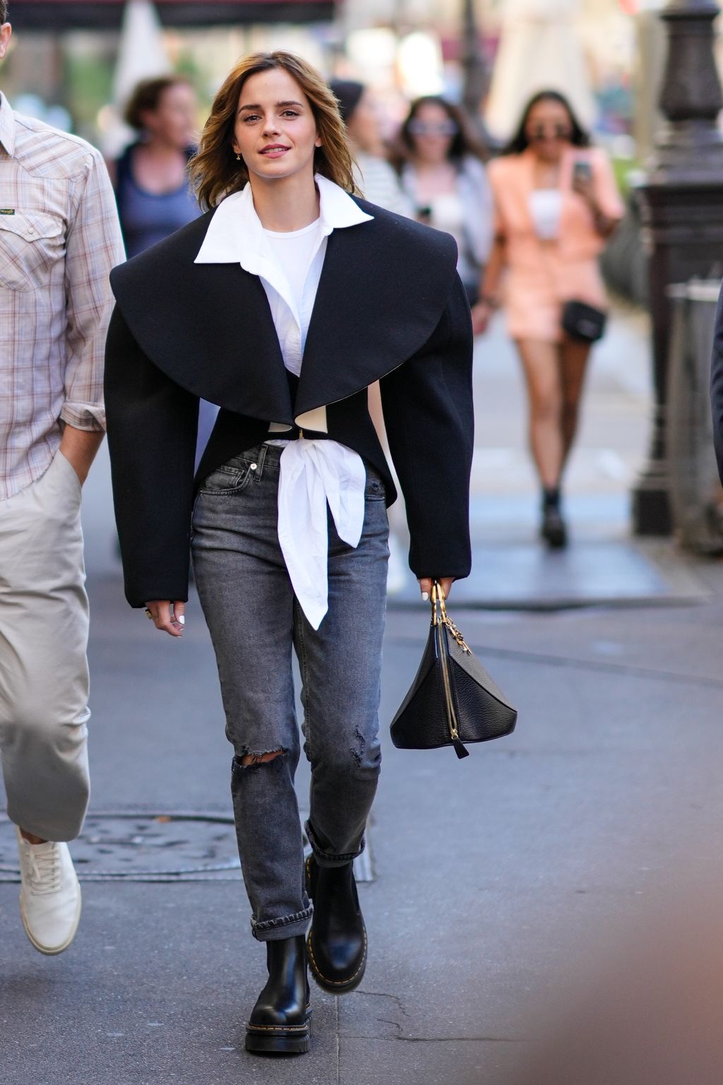 PARIS, FRANCE - JULY 04: Emma Watson wears a white t-shirt, a white oversized / cropped shirt, a black oversized epaulets / shoulder-pads cropped jacket, gray denim ripped skinny pants, black shiny leather ankle boots from Dr Martens, a black shiny leather zipper handbag , outside the Schiaparelli show, during Paris Fashion Week - Haute Couture Fall Winter 2022 2023, on July 04, 2022 in Paris, France. (Photo by Edward Berthelot/Getty Images)