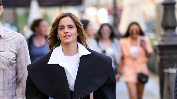 PARIS, FRANCE - JULY 04: Emma Watson wears a white t-shirt, a white oversized / cropped shirt, a black oversized epaulets / shoulder-pads cropped jacket, gray denim ripped skinny pants, black shiny leather ankle boots from Dr Martens, a black shiny leather zipper handbag , outside the Schiaparelli show, during Paris Fashion Week - Haute Couture Fall Winter 2022 2023, on July 04, 2022 in Paris, France. (Photo by Edward Berthelot/Getty Images)