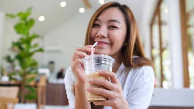 Portrait image of a beautiful young asian woman holding and drinking iced coffee in cafe