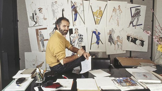 Italian fashion designer and entrepreneur Gianni Versace sitting on the table of his study. Some sketches hang on the wall. Italy, 1985 (Photo by Angelo Deligio/Mondadori via Getty Images)