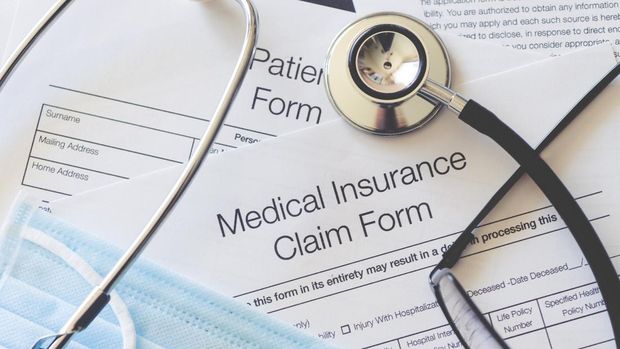 Medical Insurance claim form with stethoscope and surgical face mask. There are also other pieces of paperwork on the desk including a patient form